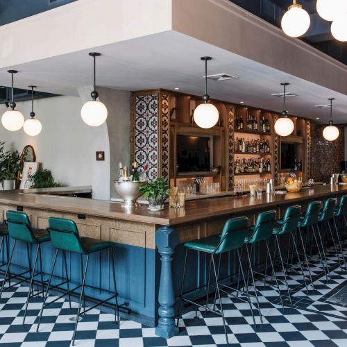 A seaside bar with a thatched roof, string lights, and a pool in front; people lounge and enjoy drinks at sunset.