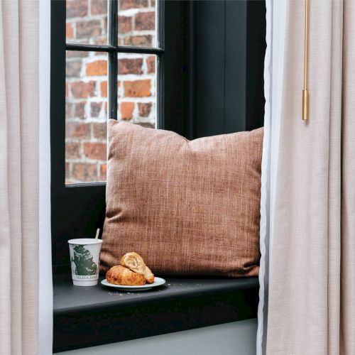 A tiny orange kitten perched on a windowsill, looking out from a sunlit room.